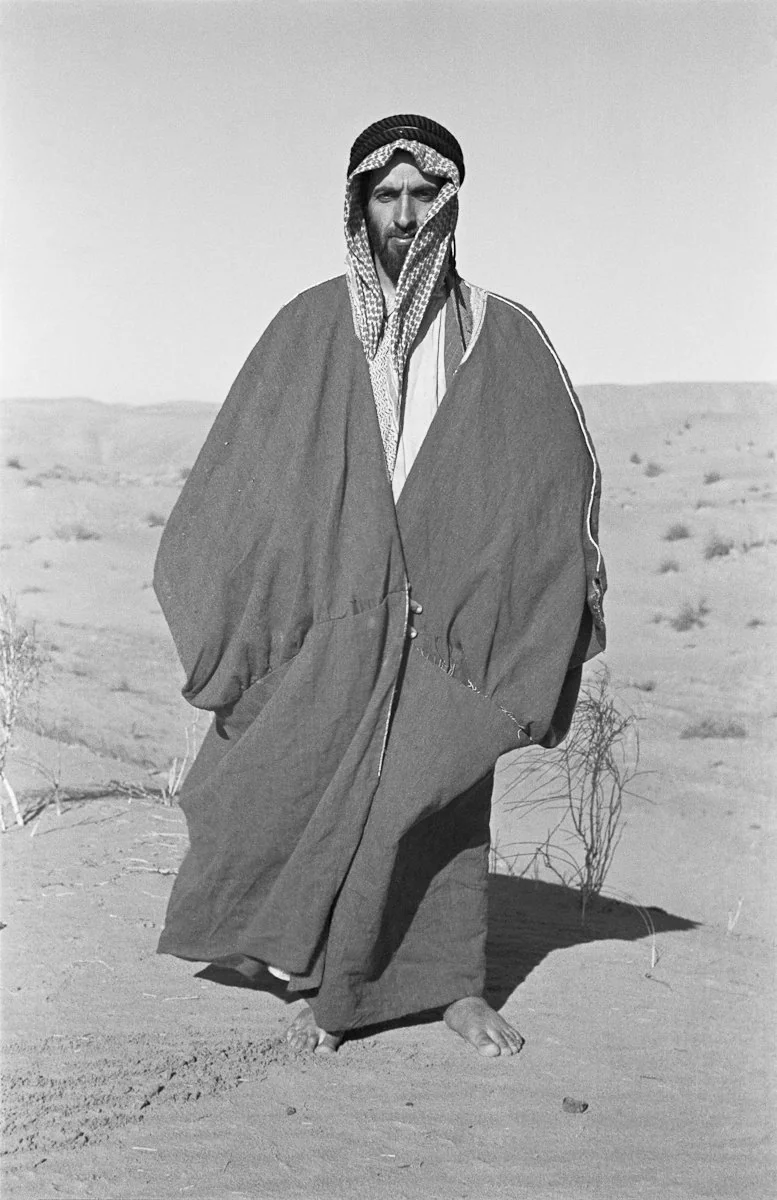 Sheikh Zayed standing barefoot in the desert, black-and-white photograph